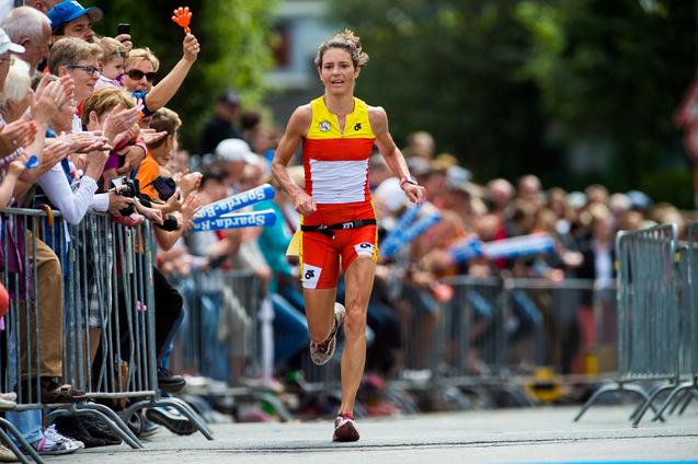 Eine Athletin in einem farbenfrohen Sportanzug sprintet an einer jubelnden Menschenmenge vorbei.